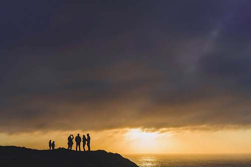 holding hands six people standing on mountain cliff at golden hour sunrise